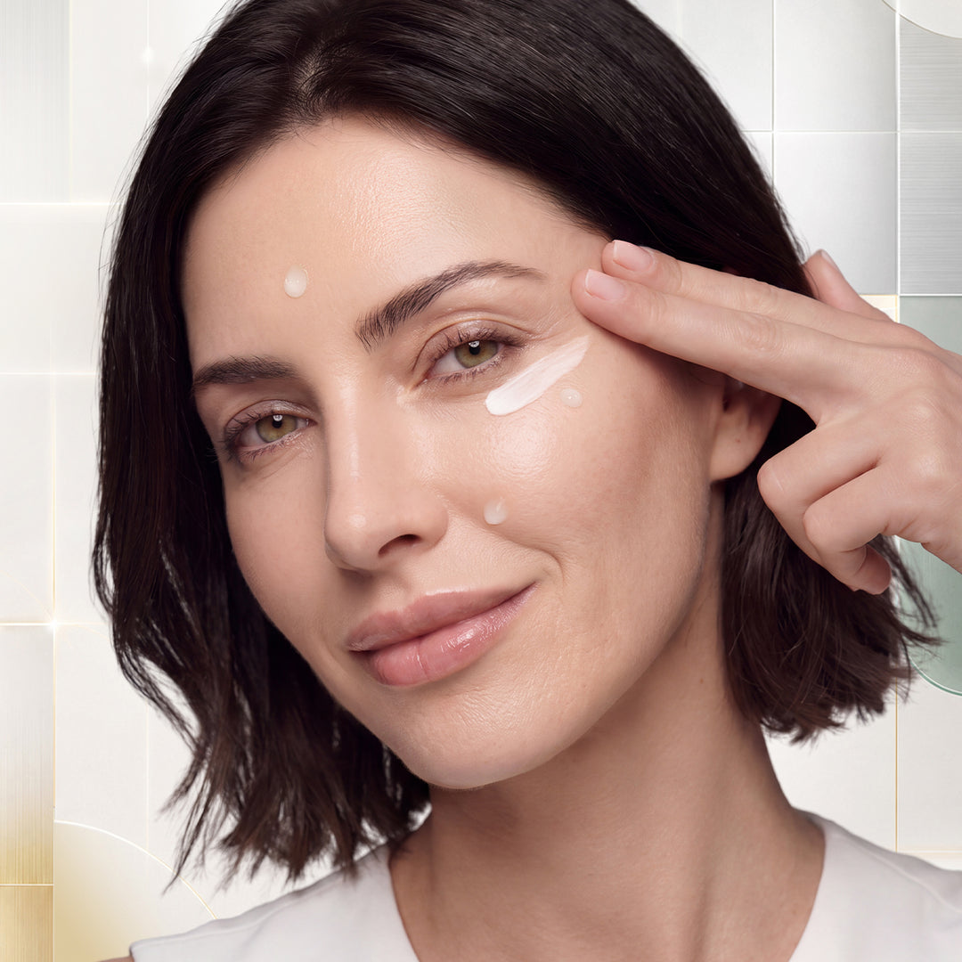 Close-up of a woman with short dark hair applying HOLIDAY SET - Intensité Set to her cheek, with a soft-focus tiled background.